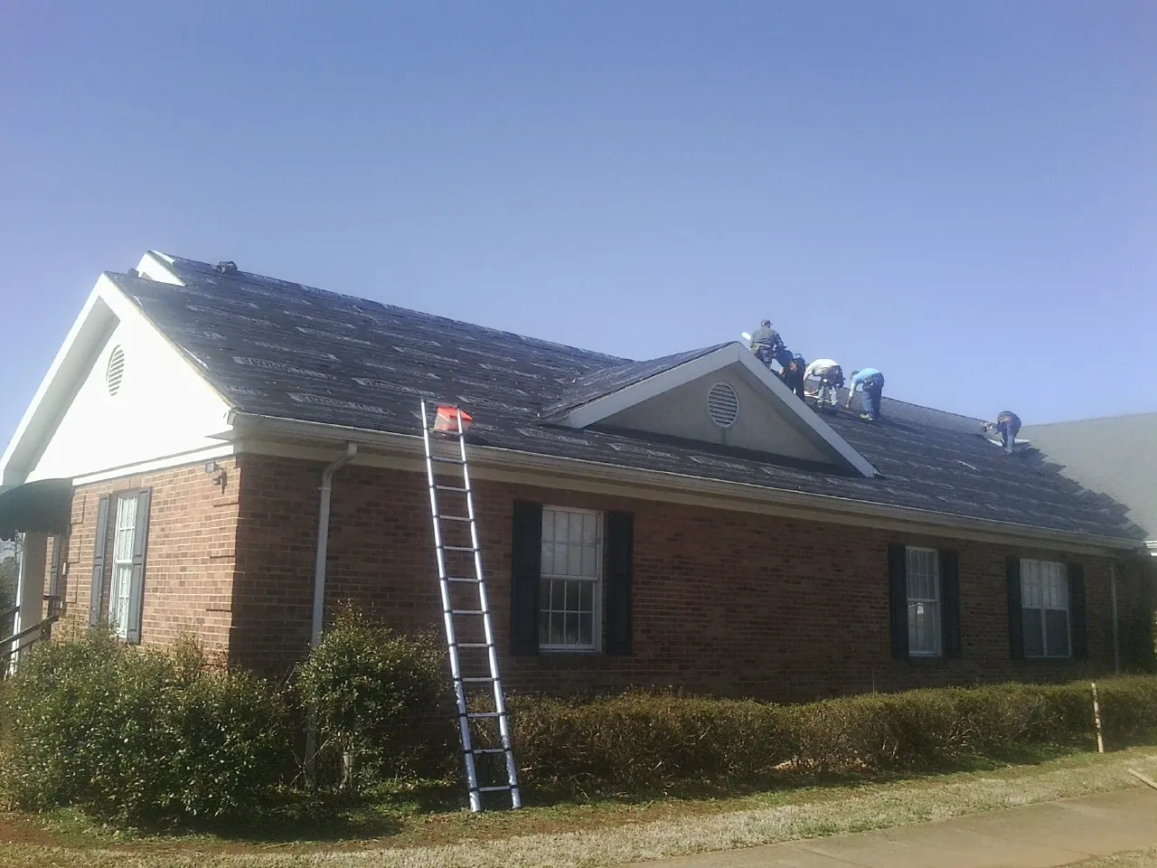 Crew tearing shingles off a brick ranch roof with a ladder set — Metal Roof Repair work by our crew in Wassaic