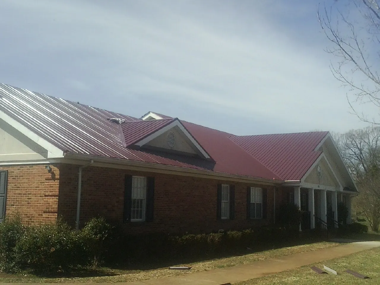 Red metal roof with gabled entries on a long brick building, from a Hail Damage Roof Repair job in Wassaic