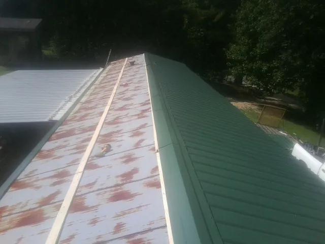 Old rusted panels beside newly installed green metal roofing — Wind Damage Roof Repair by Roofing Brothers in Wassaic