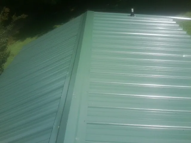 New green metal panels meeting at the ridge of a roof — Flat Roof Repair work by our crew in Wassaic