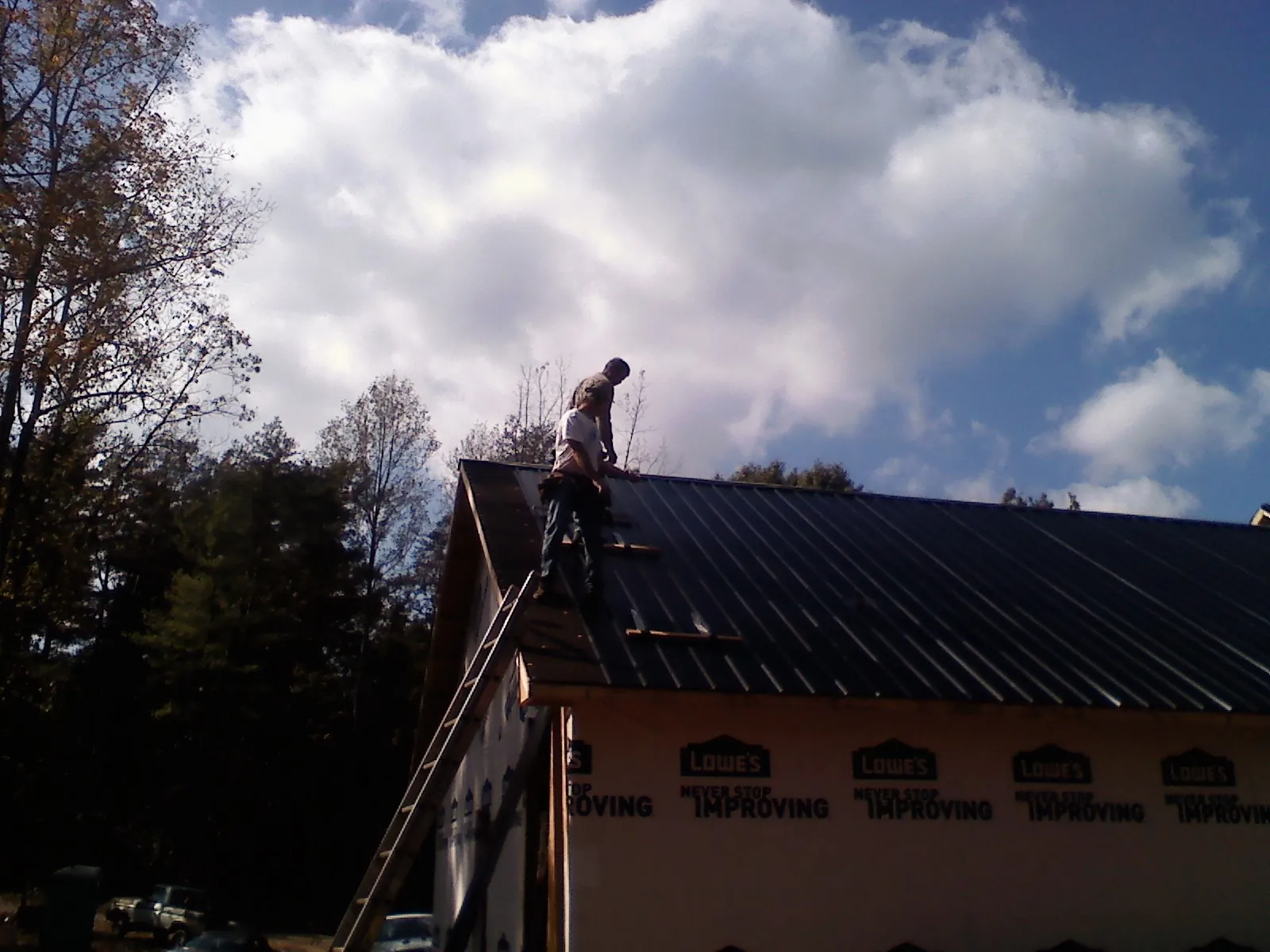 Roofer fastening dark metal panels high against a cloudy sky, from a Roof Inspection job in Wassaic