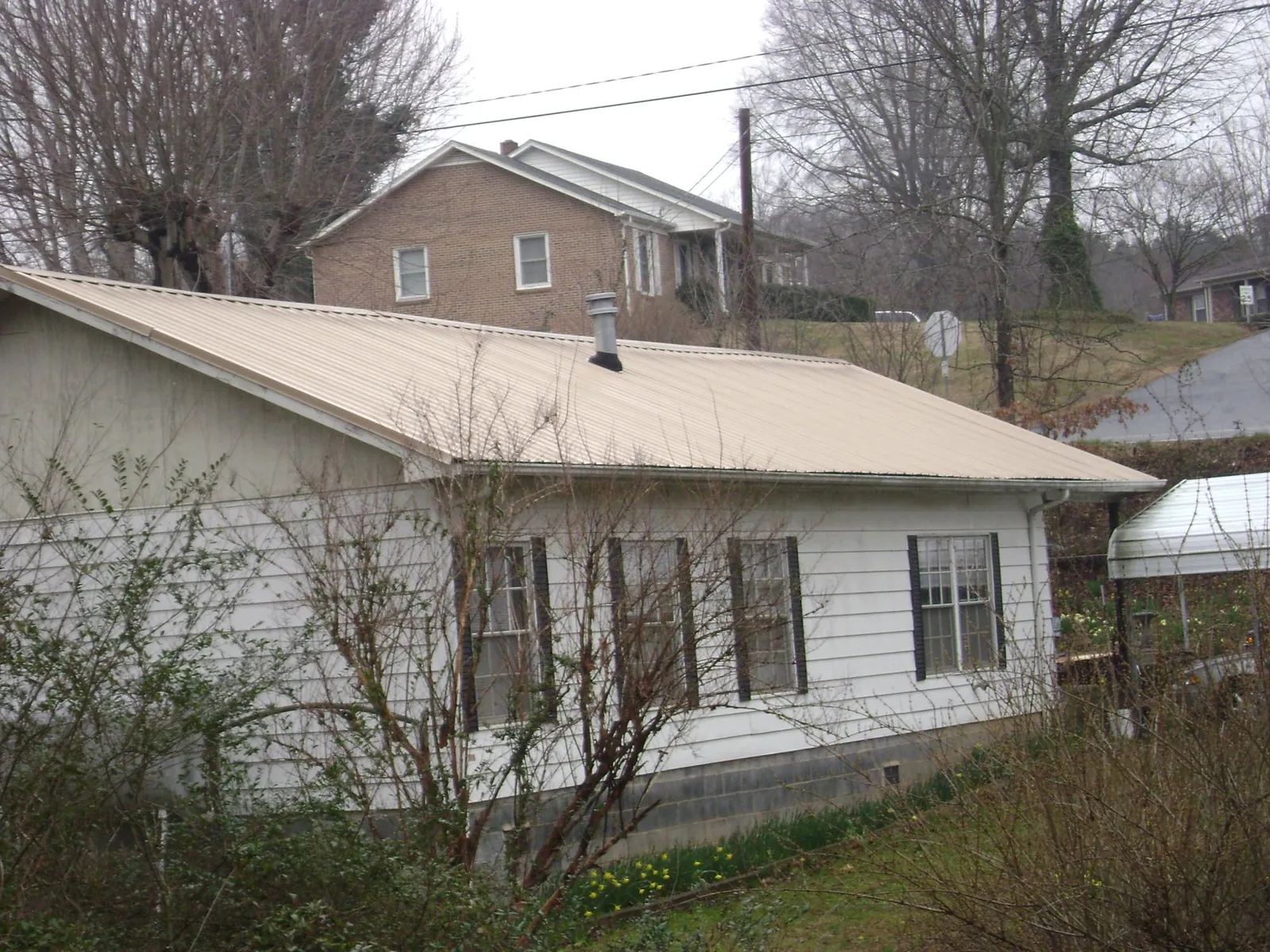 Tan metal roof on a white sided house set into a hillside — Commercial Roofing by Roofing Brothers in Wassaic